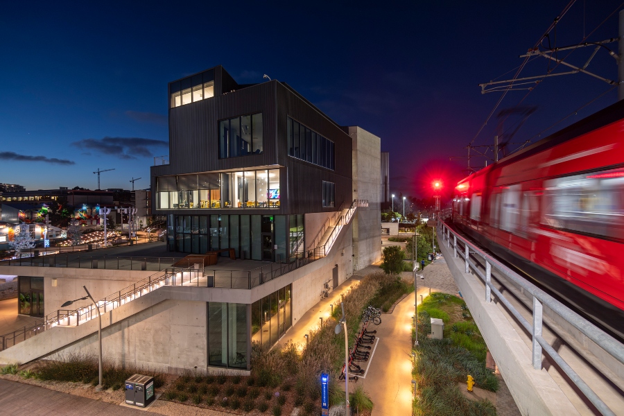 The Design and Innovation Building at night, surrounded by a lit up path and trolley whizzing by.