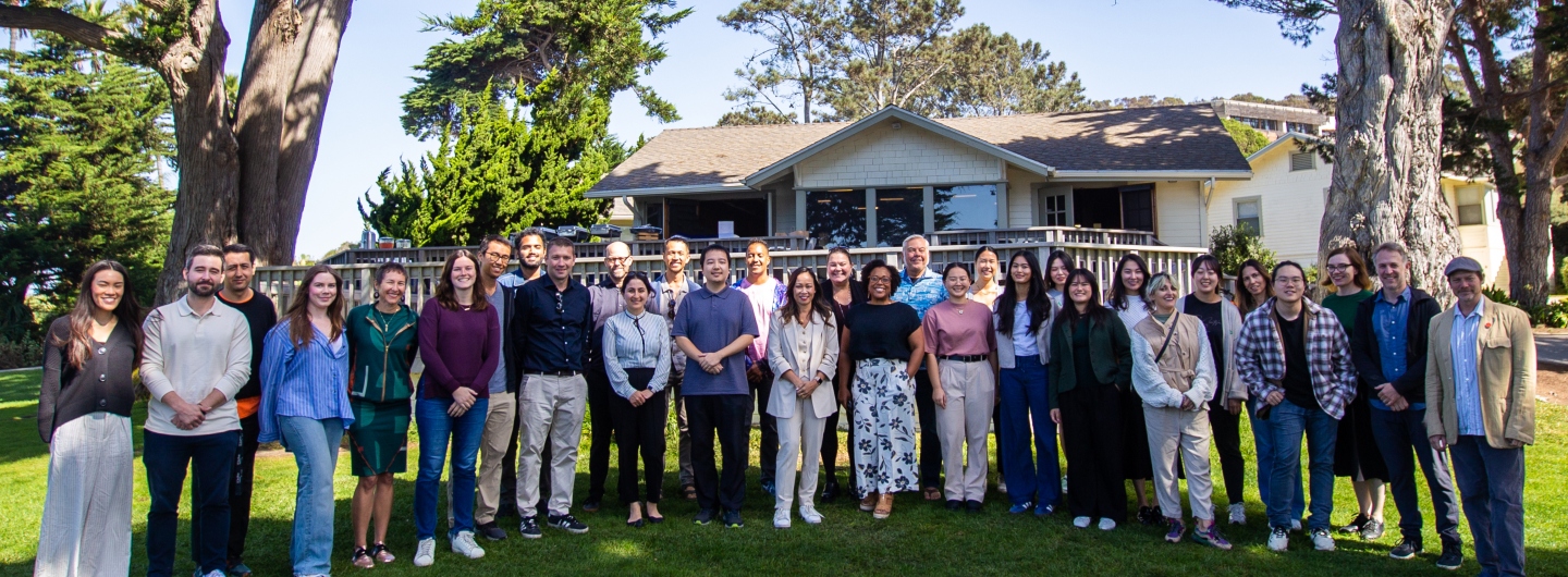 Group of members at the Design Lab Retreat 2024. Standing in a line in the grass in front of a house.