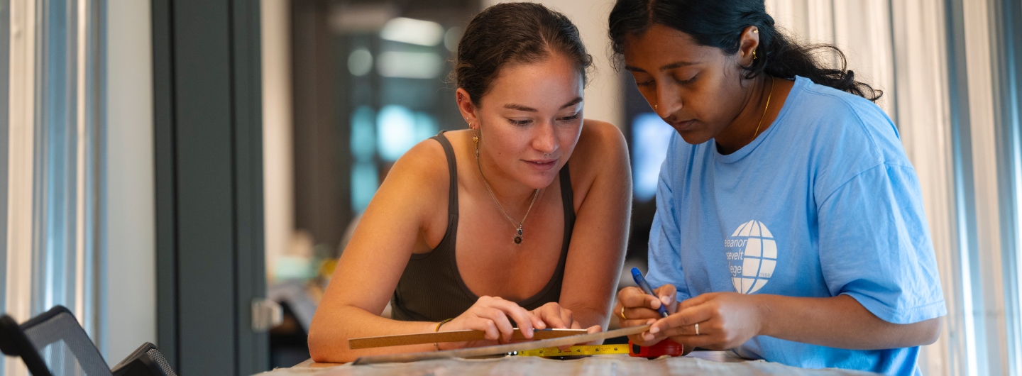 Two students working on a project by carefully measuring material.